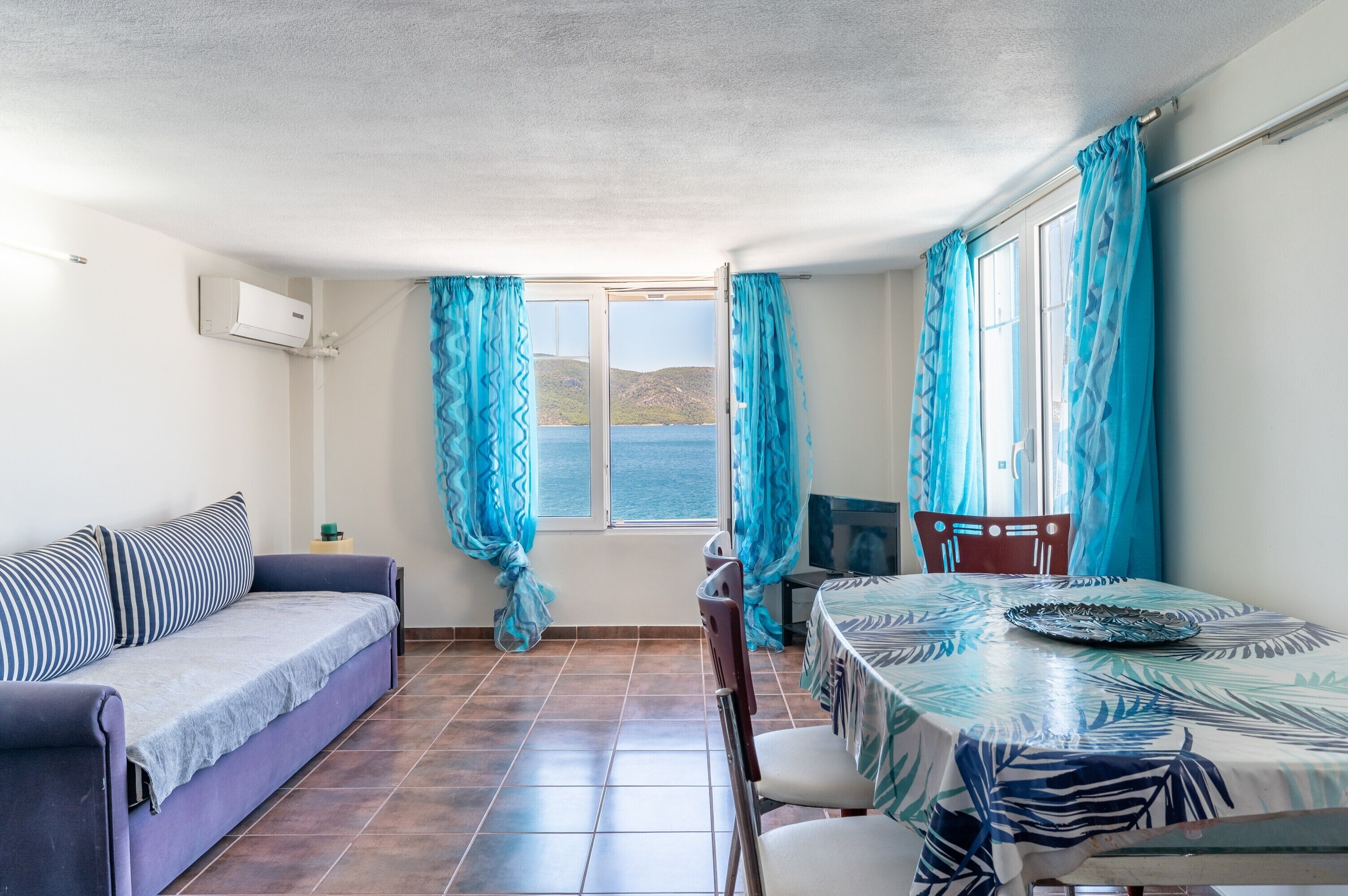 A room with a sofa, a dining table, a chair, and a window with curtains.