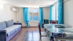 A room with a sofa, a dining table, a chair, and a window with curtains. - Apartment 'Apollonas' with Sea View, Wi-Fi and Air Conditioning (Salamina)