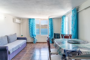 A room with a sofa, a dining table, a chair, and a window with curtains. - Apartment 'Apollonas' with Sea View, Wi-Fi and Air Conditioning (Salamina)