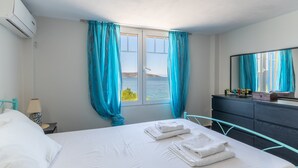 A hotel room with a bed, a nightstand, a lamp, a dresser, a mirror, and a window with curtains. - Apartment 'Apollonas' with Sea View, Wi-Fi and Air Conditioning (Salamina)