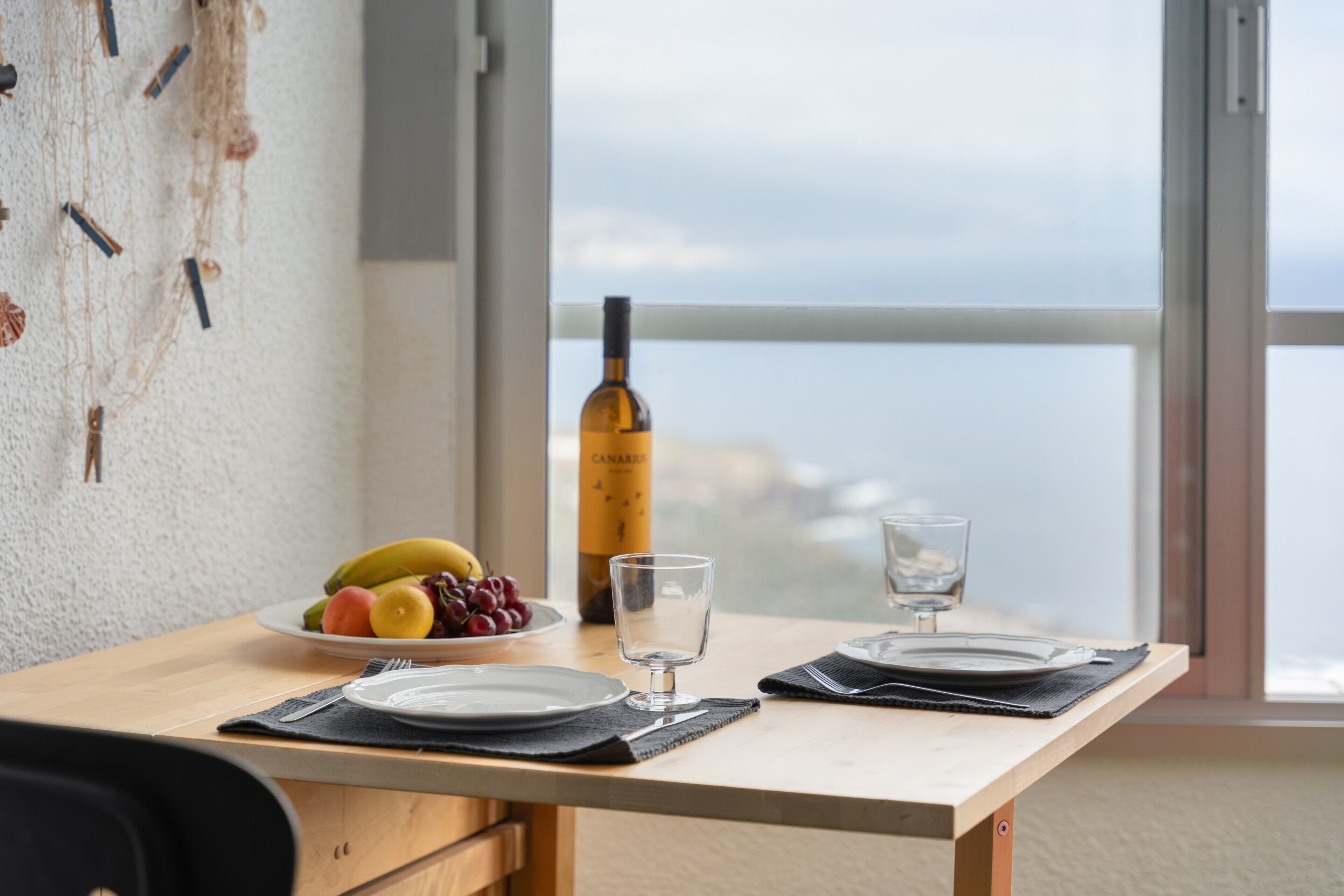 Una mesa de comedor con platos, cubiertos, una botella de vino y un frutero.