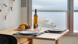 A dining table with plates, cutlery, a wine bottle, and a fruit bowl. - 'The Blue Lighthouse' Studio with Sea View, Shared Pool, and Wi-Fi (La Matanza de Acentejo)