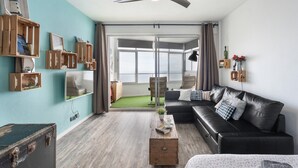 A modern living room with a black leather sofa, wooden shelves, and a ceiling fan. - 'The Blue Lighthouse' Studio with Sea View, Shared Pool, and Wi-Fi (La Matanza de Acentejo)