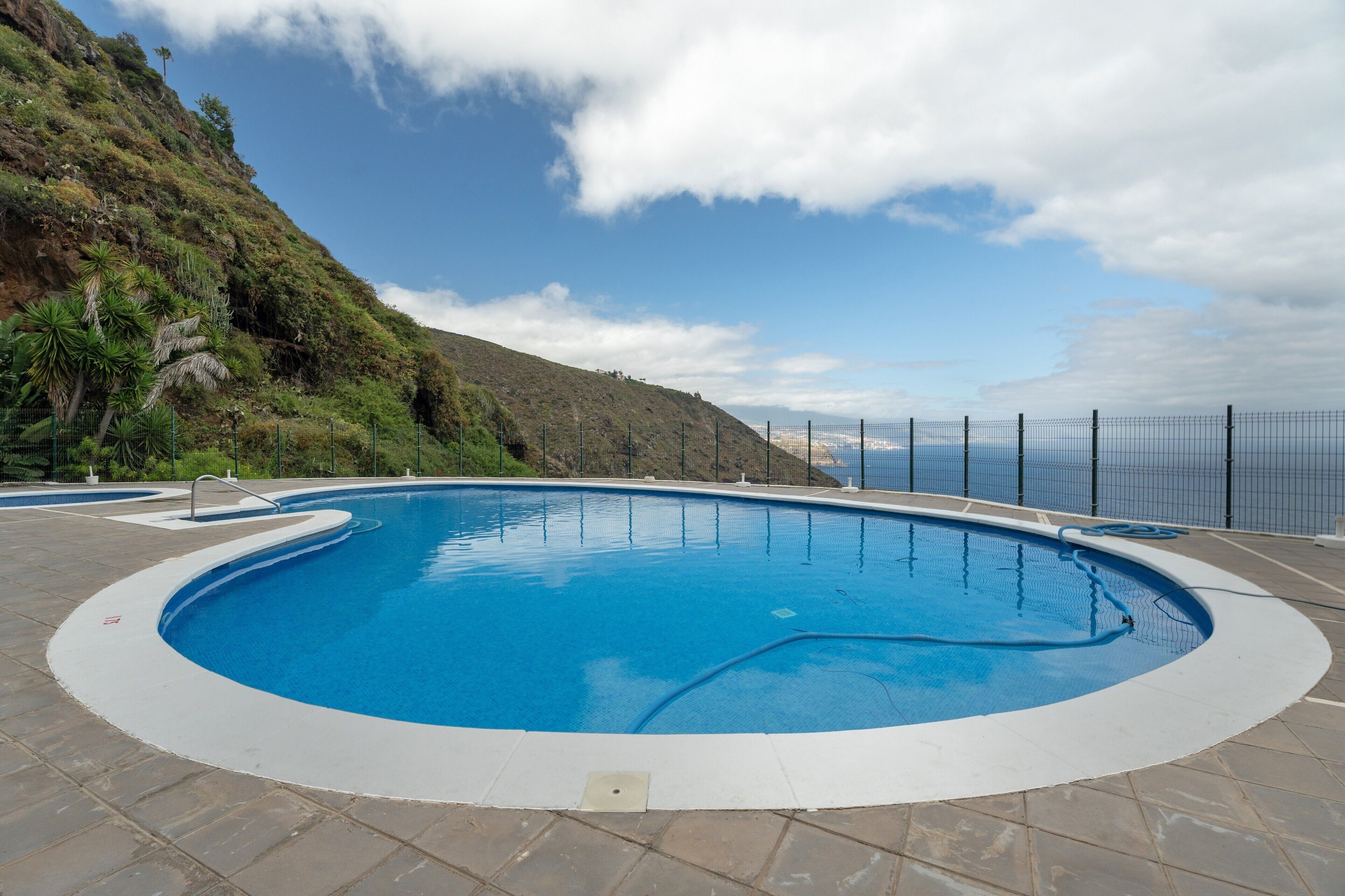 Una piscina con borde curvo, rodeada por una solana con baldosas y vista a un paisaje montañoso.