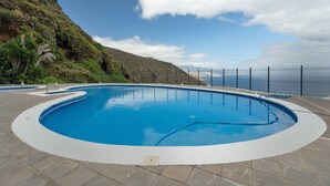 A swimming pool with a curved edge, surrounded by a tiled deck, and a view of a mountainous landscape. - 'The Blue Lighthouse' Studio with Sea View, Shared Pool, and Wi-Fi (La Matanza de Acentejo)