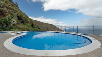 Una piscina con borde curvo, rodeada por una solana con baldosas y vista a un paisaje montañoso.