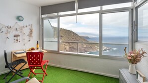 A room with a large window, a desk, two chairs, a small table with a vase, and a green carpet. - 'The Blue Lighthouse' Studio with Sea View, Shared Pool, and Wi-Fi (La Matanza de Acentejo)