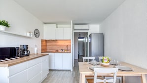 Eine moderne Küche mit weißen Schränken, einer Mikrowelle und einer Kaffeemaschine. Es gibt einen Essbereich mit einem Holztisch und Stühlen.