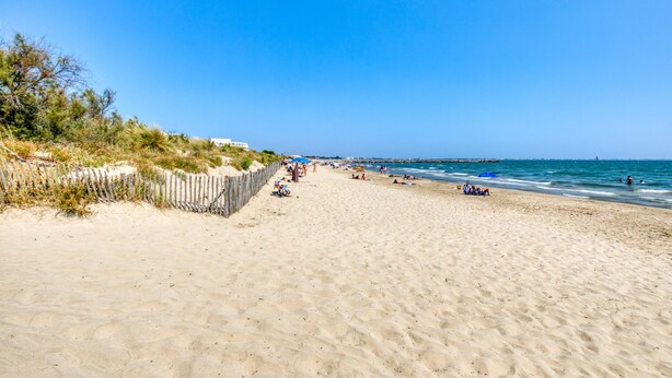 Ein Strand mit einer Holzzaun, entspannten Menschen und blauem, wolkenlosem Himmel.