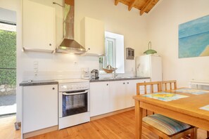 Uma cozinha compacta com armários brancos, forno embutido e um espaço de refeições com mesa e cadeiras de madeira.