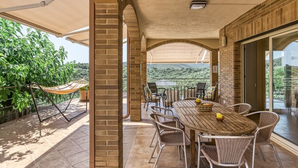 Une terrasse extérieure avec une table et des chaises en bois, un hamac et une vue sur un paysage naturel.