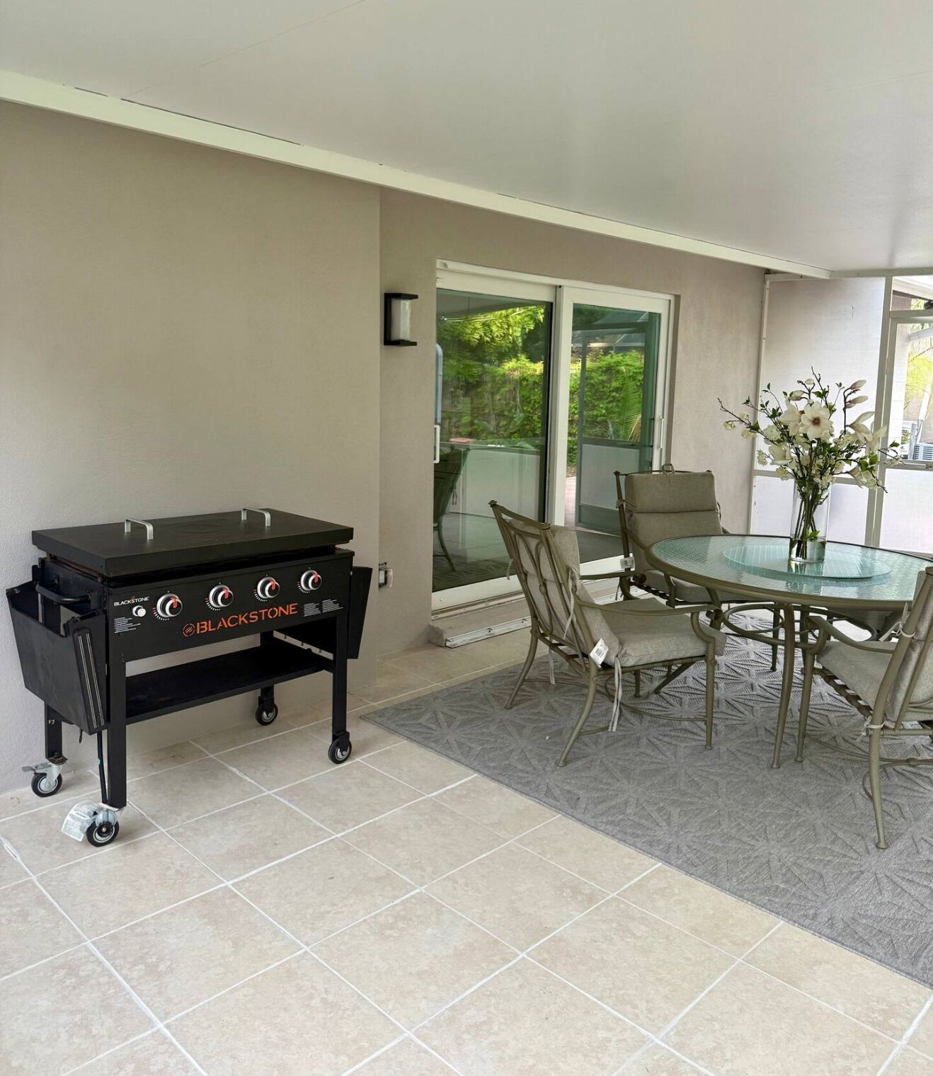 A patio area with a barbecue grill, a round glass table, and chairs.