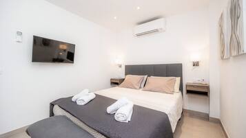 A modern hotel room with a large bed, bedside tables, a flat-screen TV, an air conditioning unit, and artwork on the wall.