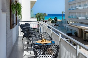 Een balkon met een tafel en stoelen, met uitzicht op een strand en een gebouw met meerdere verdiepingen.
