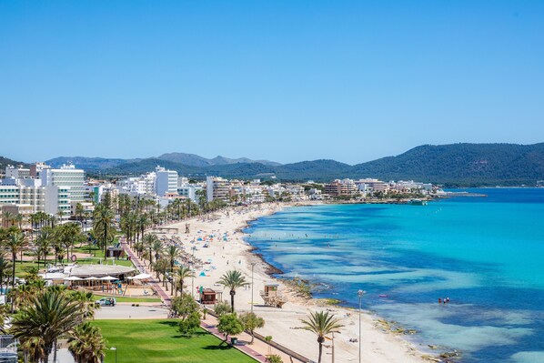 A coastal cityscape with a beach, buildings, and mountains in the background.