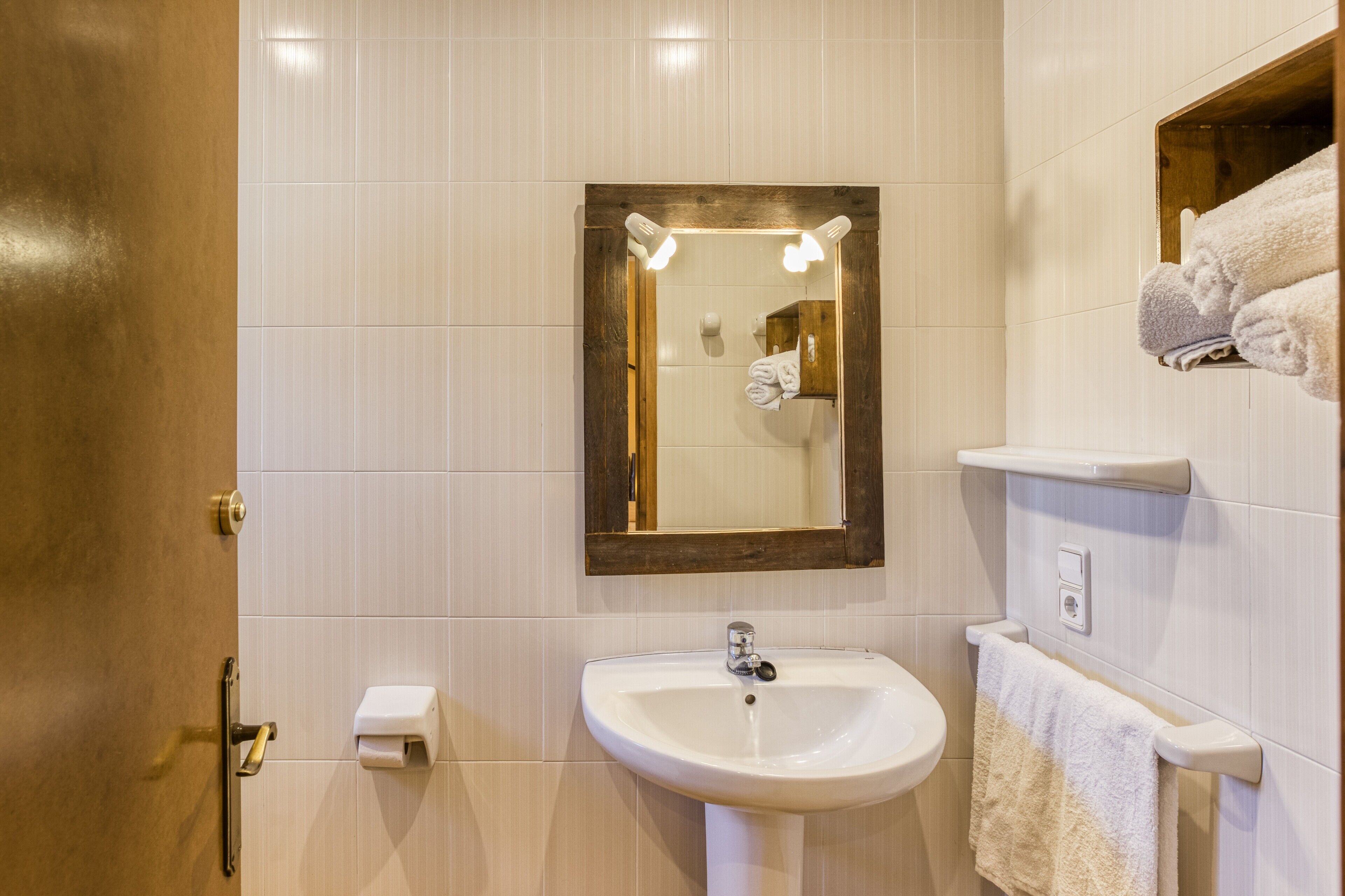A bathroom with a sink, mirror, towel rack, and a wooden door.