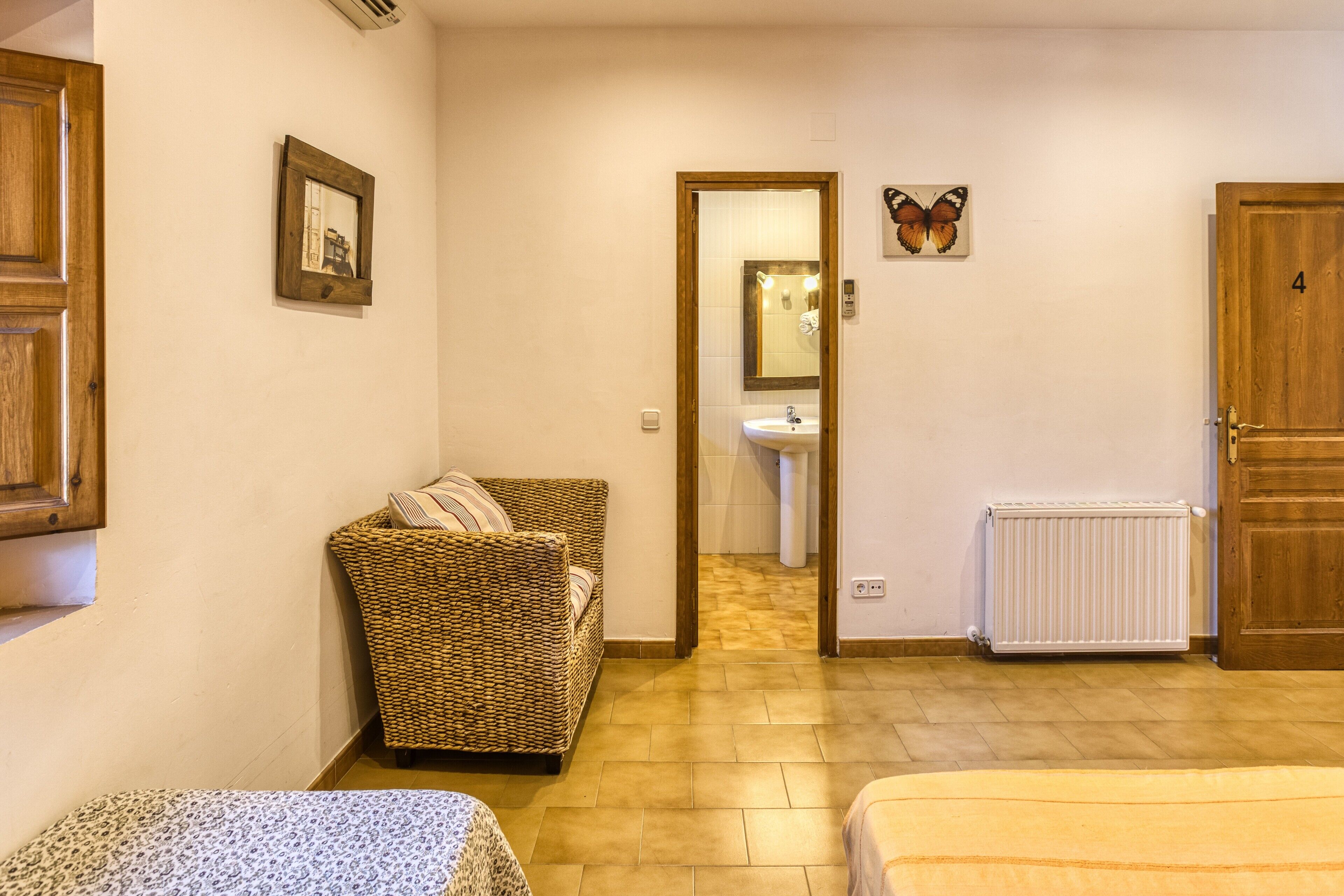 Una stanza con un letto, un divano in vimini, uno specchio e un termosifone.