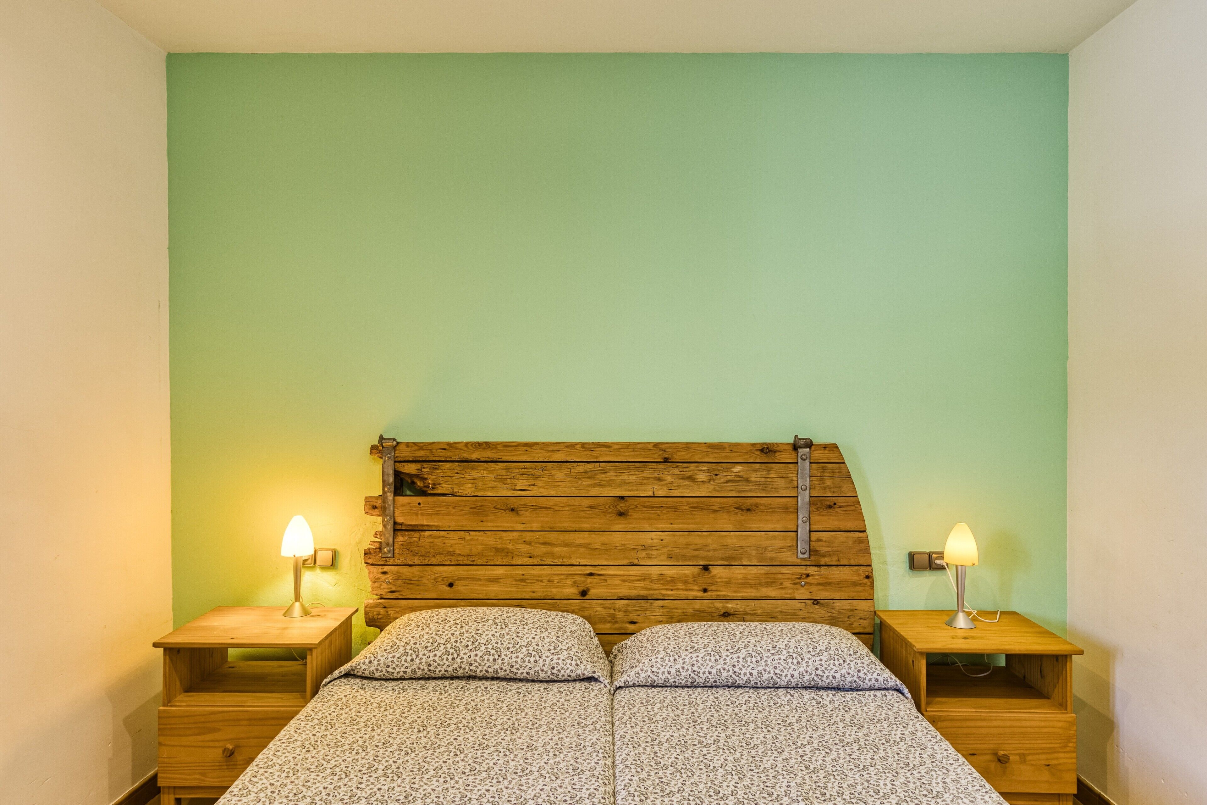 Una cama doble con cabecera de madera, dos mesitas de noche con lámparas y una pared verde.
