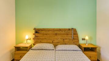 Una cama doble con cabecera de madera, dos mesitas de noche con lámparas y una pared verde.