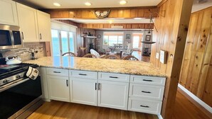 A kitchen with wooden cabinets, a granite countertop, and a stainless steel stove. - Relax and unwind at this 3-bedroom bayfront house in charming Mattituck. (Mattituck)