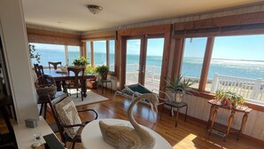 A spacious living room with a large window overlooking the sea, furnished with a round table, chairs, and a decorative swan sculpture. - Relax and unwind at this 3-bedroom bayfront house in charming Mattituck. (Mattituck)