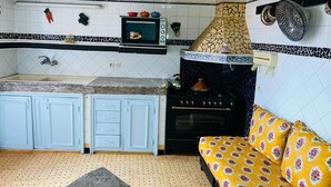 A compact kitchen with a microwave, stove, and sink. There is a patterned sofa with cushions.