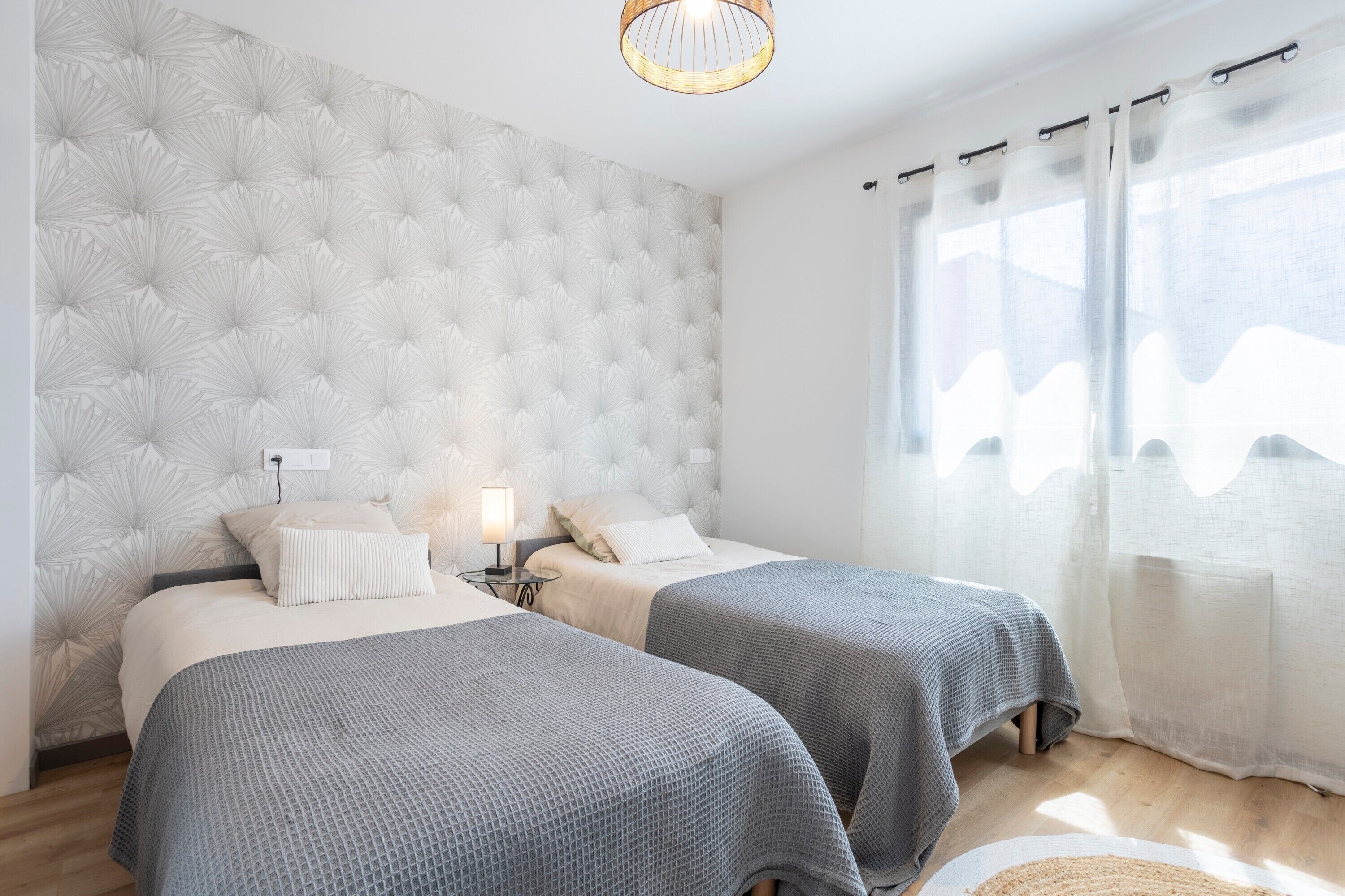 A bedroom with two beds, a tufted headboard, bedside lamps, and sheer curtains.