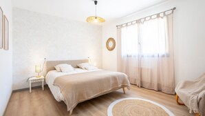 Un dormitorio con cama, mesitas de noche, una lámpara colgante, un tapete redondo y una ventana con cortinas.