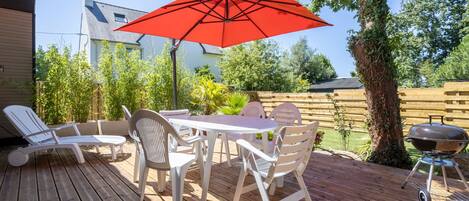 Eine Holzterrasse mit Tisch und Stühlen, einem roten Sonnenschirm und einem Grill.