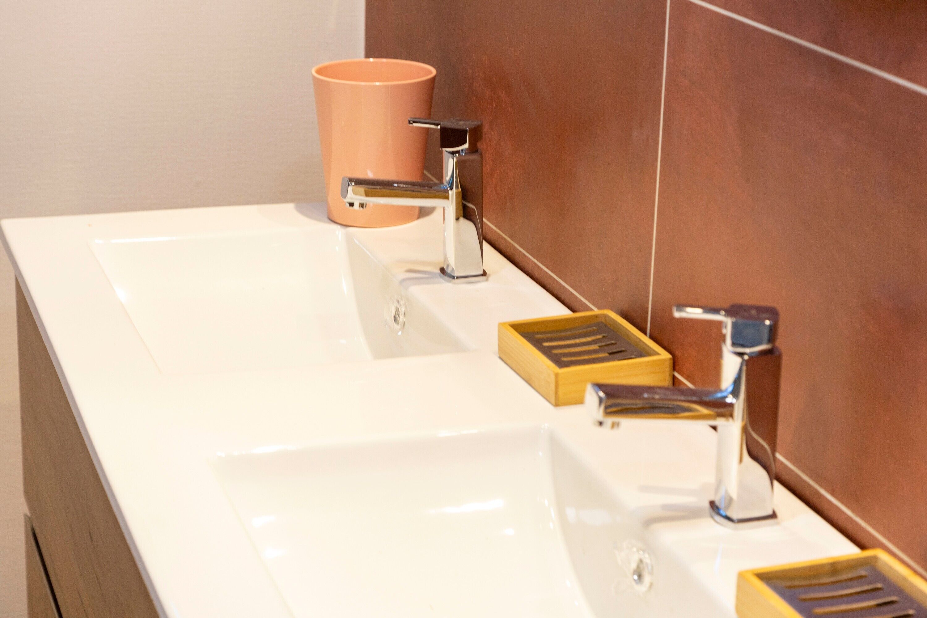 Une salle de bain avec un lavabo blanc, deux robinets en chrome et un porte-savon en bois.