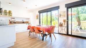 Cocina moderna con armarios blancos, una mesa de comedor con sillas naranjas y ventanas amplias que ofrecen vistas al exterior.