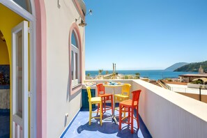A balcony with a table and chairs, a view of the sea, and a building with a pink and yellow facade. - 'Green' Room with Shared Terrace, Wi-Fi and Air Conditioning (Lipari)