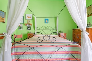 A bed with a metal frame, a striped bedspread, and white curtains. There are wall decorations and a wooden dresser.