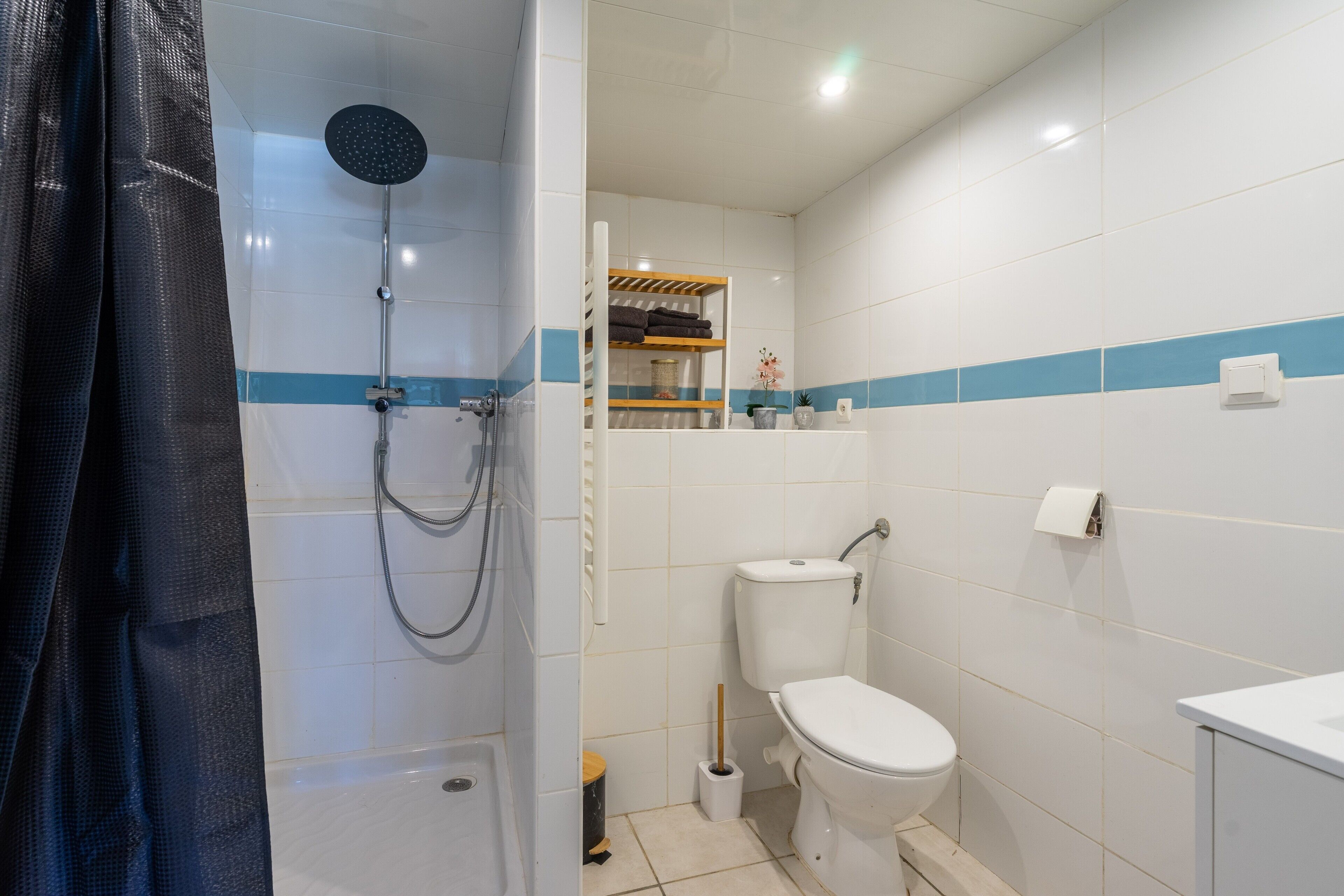 A bathroom with a shower, toilet, and a shelf with towels.