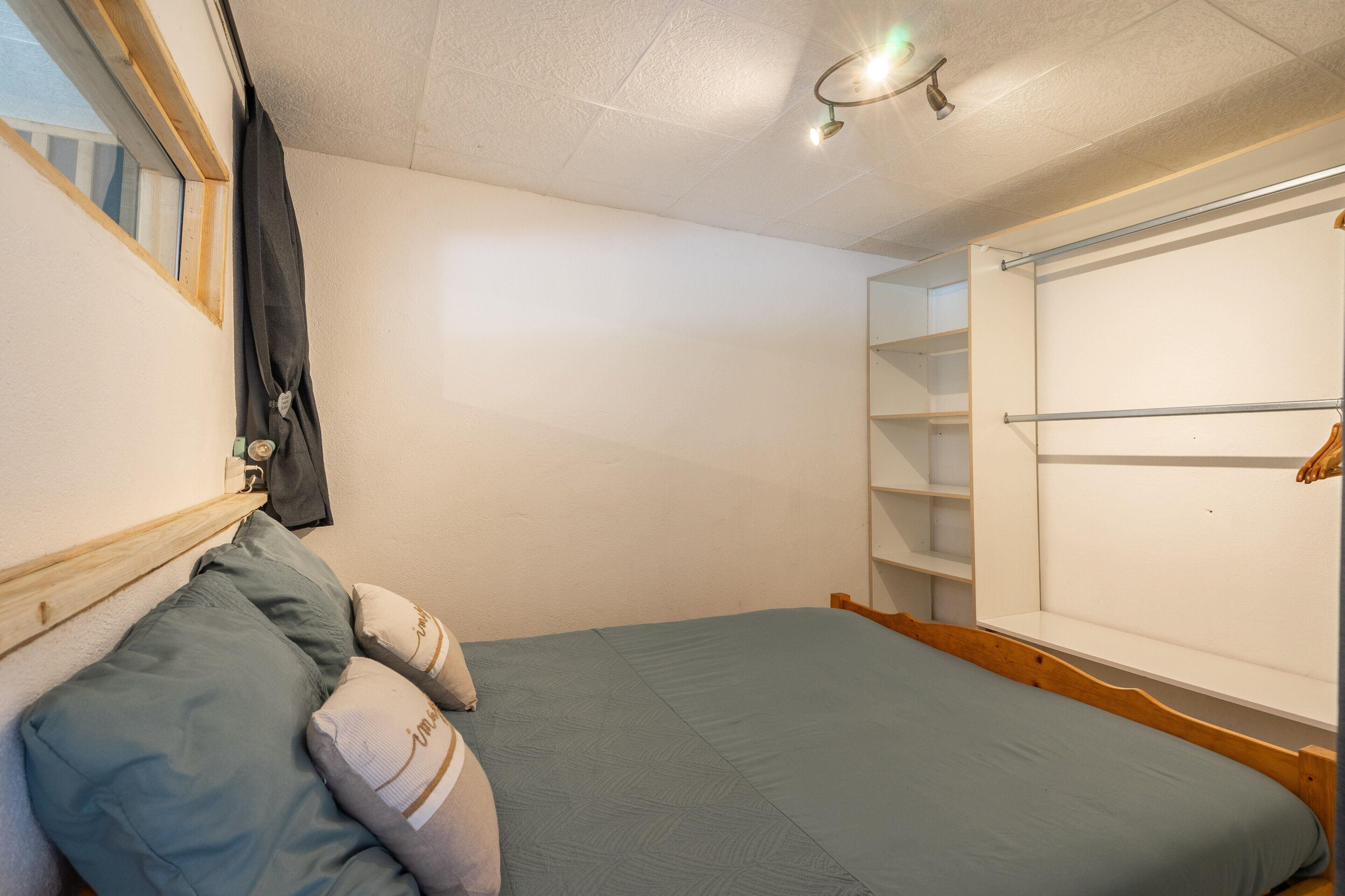 A bedroom with a bed, pillows, a shelf unit, and a window.