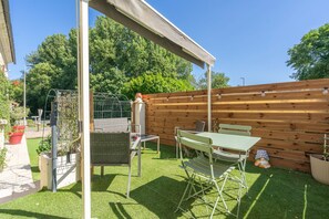 Ein überdachter Patio-Bereich mit Tisch und Stühlen, ein Holzzaun und ein Garten mit Topfpflanzen.
