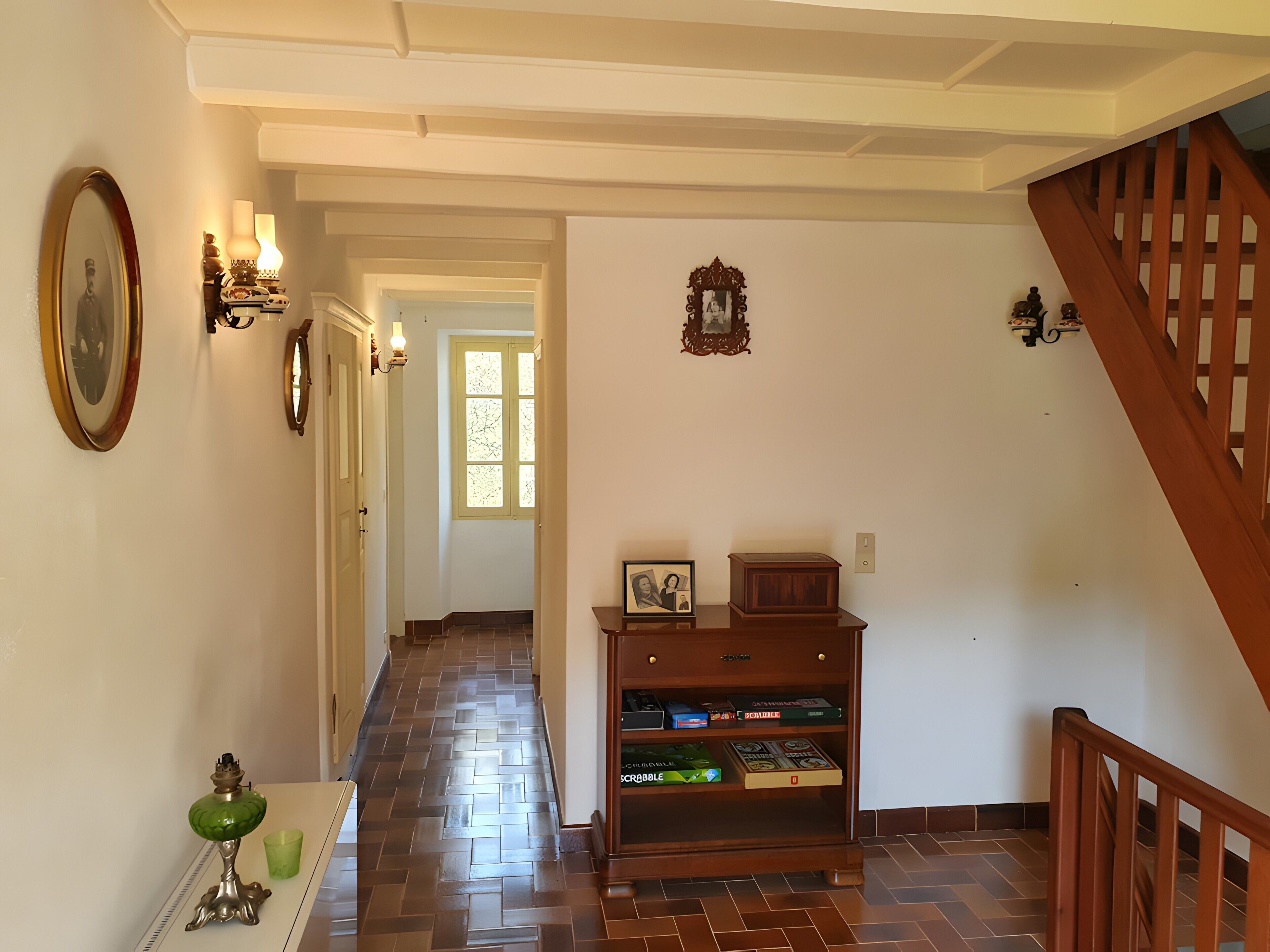 A hallway with a wooden staircase, a wall-mounted shelf with books, and a green decorative item.