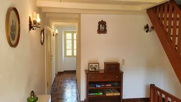 A hallway with a wooden staircase, a wall-mounted shelf with books, and a green decorative item.