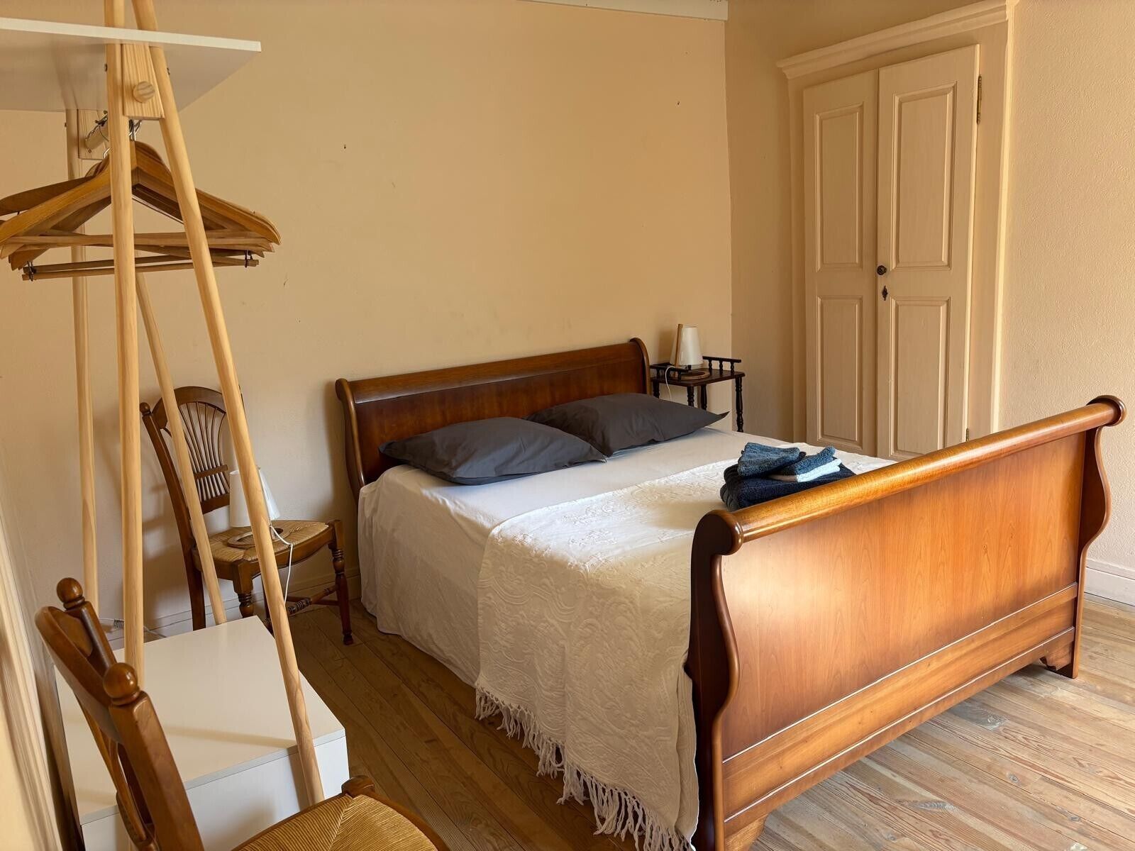 Ein Schlafzimmer mit einem hölzernen Bett, einem Hängesessel, einem Nachttisch und einer Tür.