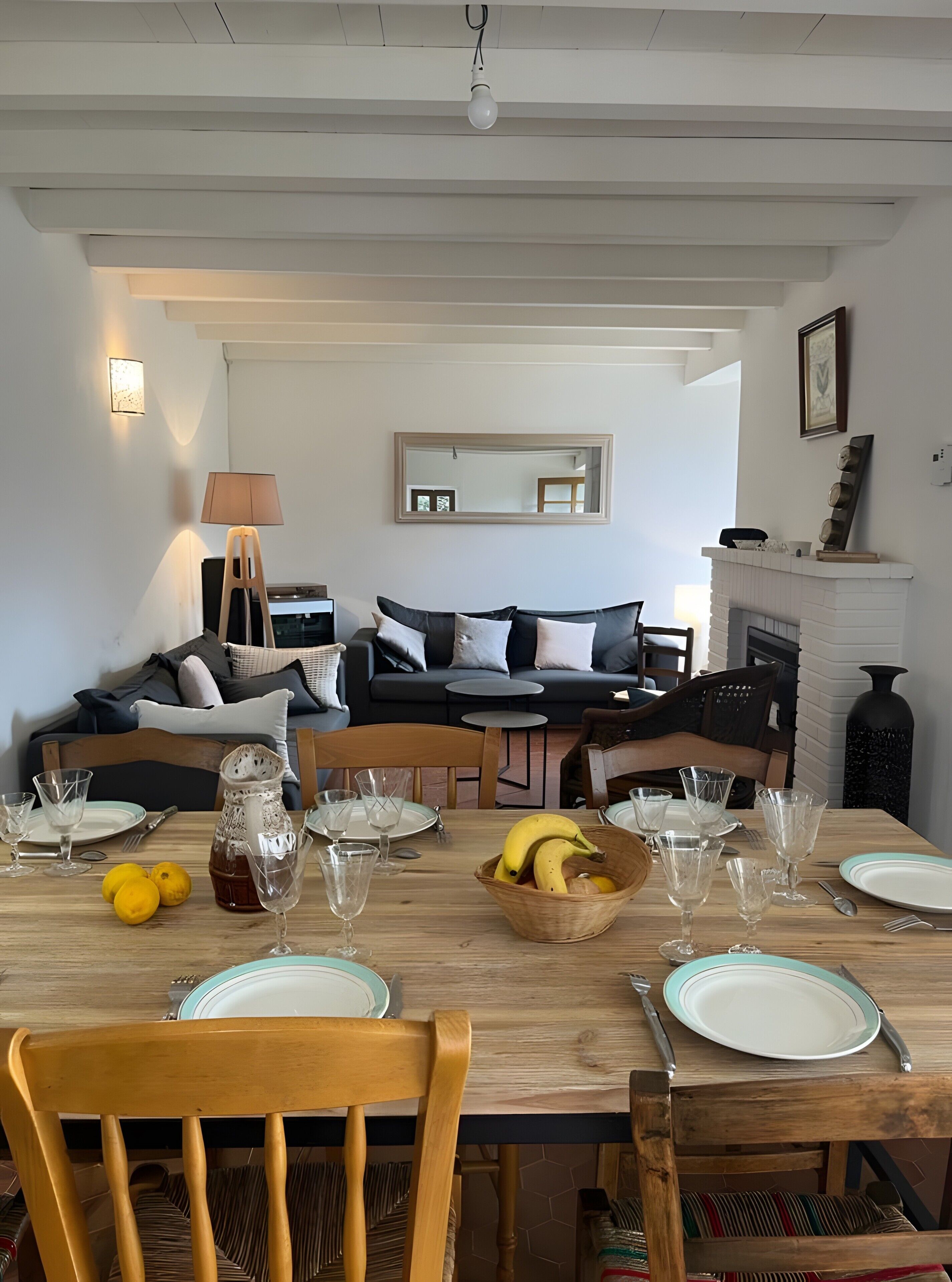 A dining area with a wooden table set for a meal, a sofa in the background, and a fireplace.