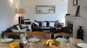 A dining area with a wooden table set for a meal, a sofa in the background, and a fireplace.