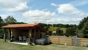 A rustic outdoor seating area with a covered patio, a wooden fence, and a lake in the background. - Porcherat - Perigord Vert, Dordogne: Lake View, Private Garden & Wi-Fi (La Roche-Chalais)