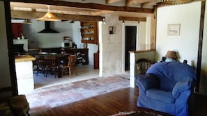 Een ruime woonkamer met een blauwe bank, houten vloeren en een keuken op de achtergrond.