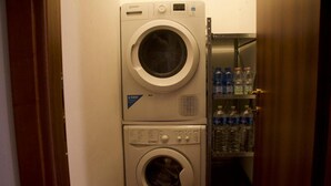 A front-loading washing machine and dryer stacked in a laundry room with a shelf of bottled water. - Apartment 'Mandiri' with Private Terrace, Balcony and Wi-Fi (San Casciano in Val di Pesa)