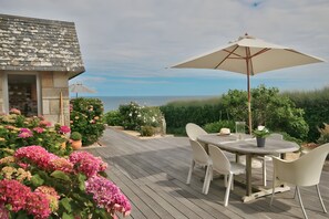 A wooden deck with a round table and chairs, a large umbrella, and a view of the sea. - Large contemporary villa, right on the water... (Audierne)