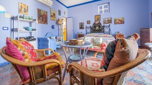 A room with a bed, wicker chairs, a small table, and a wall-mounted shelf. - Room 'Blu' with Shared Terrace, Wi-Fi and Air Conditioning (Lipari)