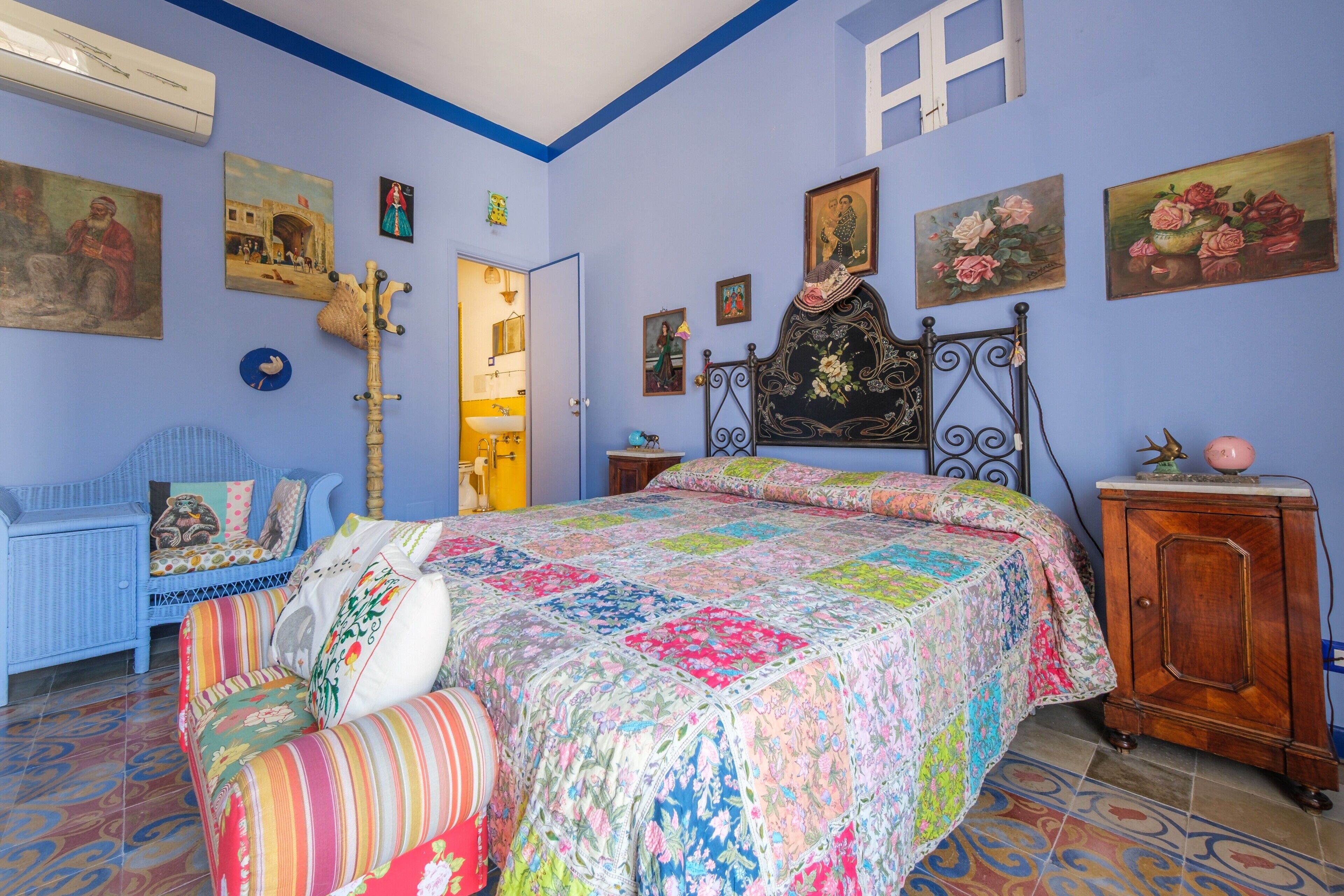 Una camera da letto con un letto, un armadietto in legno, una sedia blu e diverse decorazioni a parete.