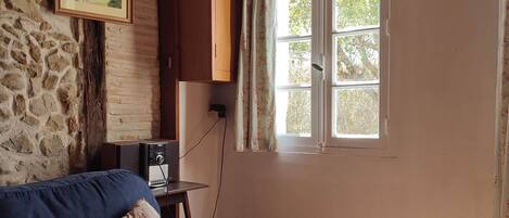 A room with a blue sofa, a stone wall, a window with curtains, and a rug on the floor.
