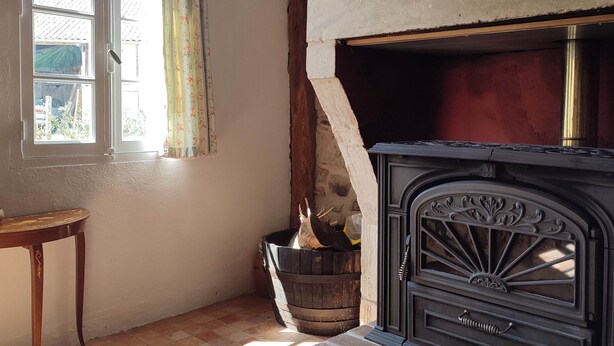 A room with a fireplace, a window with curtains, a wooden table, and a patterned rug.