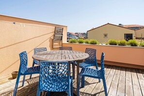 A rooftop terrace with a round wooden table and blue chairs, surrounded by a beige wall and a view of buildings. - Apartment 'Notre Dame' with Sea View, Private Terrace and Wi-Fi (Capbreton)